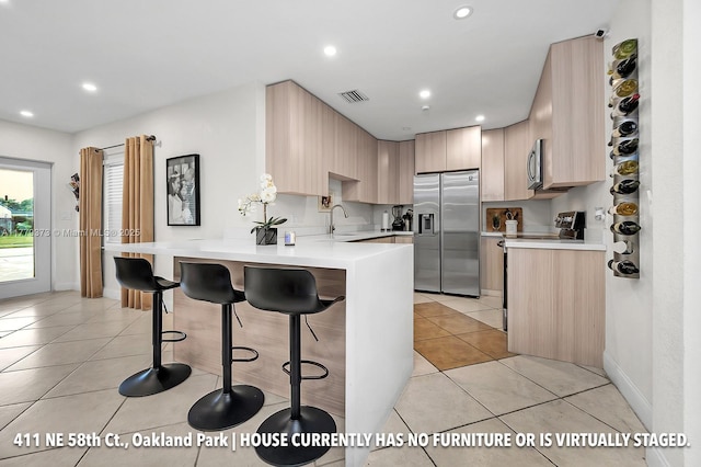 411 NE 58th Ct, Oakland Park, FL 33334 - kitchen featuring light brown cabinets, visible vents, a kitchen bar, a peninsula, and stainless steel appliances