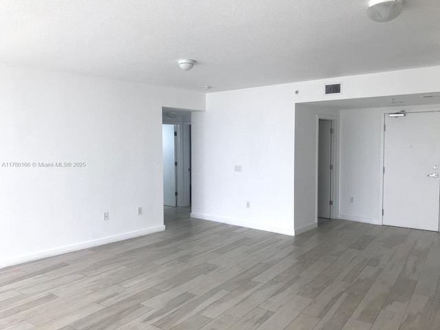 spare room with a textured ceiling, light wood finished floors, baseboards, and visible vents
