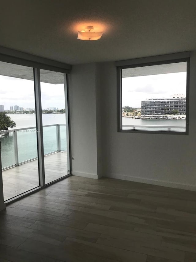 unfurnished room featuring wood finished floors, baseboards, and a water view