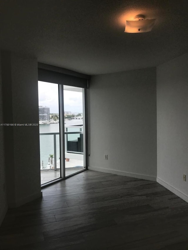 unfurnished room with a water view, baseboards, and dark wood finished floors