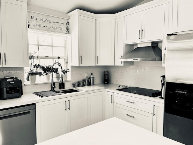 kitchen with wall chimney range hood, white cabinetry, a sink, stainless steel appliances, and light countertops