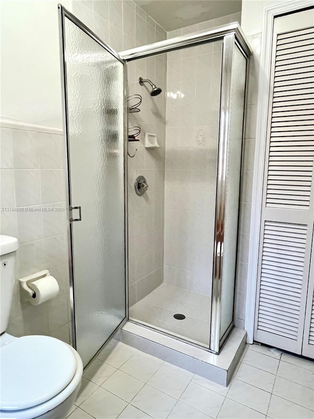 bathroom with toilet, tile patterned flooring, tile walls, and a shower stall