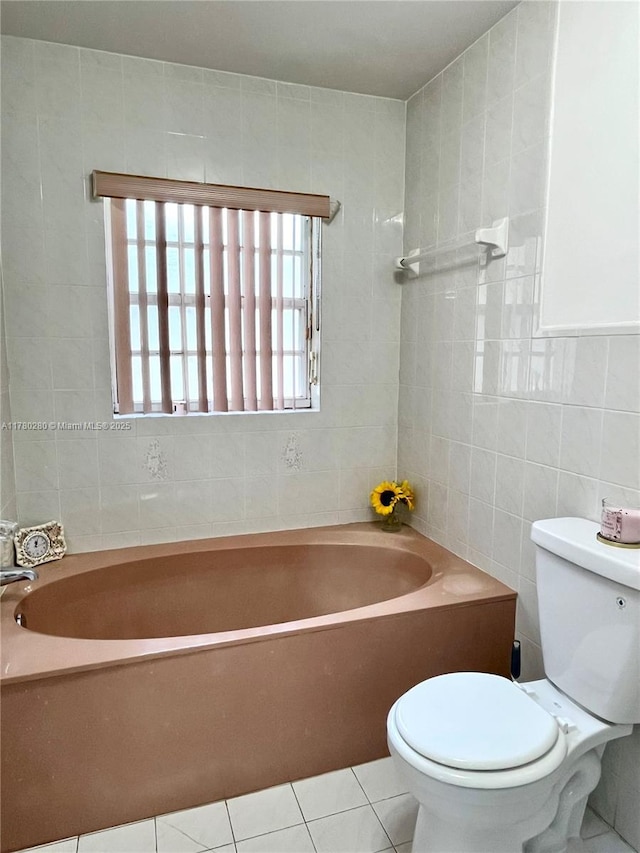 full bath featuring tile patterned floors, a tub to relax in, toilet, and tile walls
