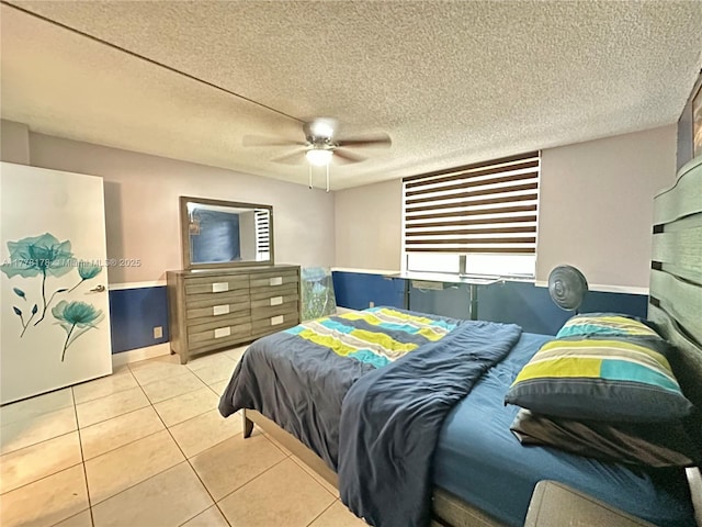 tiled bedroom with a textured ceiling, a ceiling fan, and wainscoting
