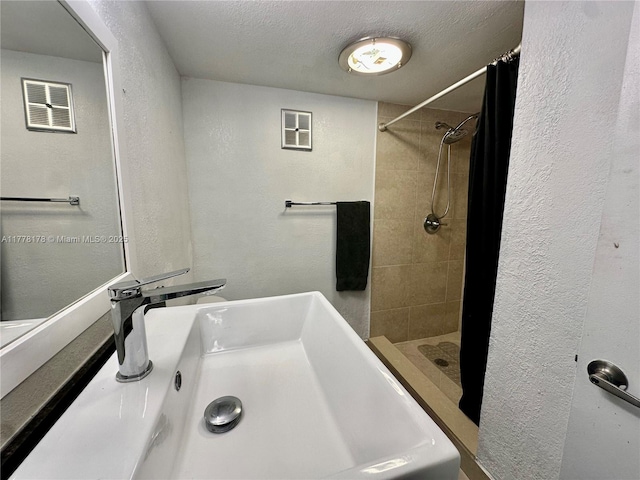 bathroom with a textured wall, visible vents, a shower stall, and a sink