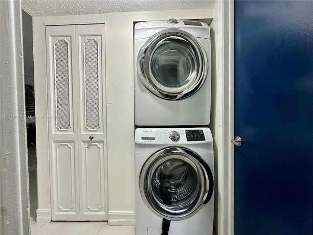 laundry room with tile patterned flooring, stacked washer / drying machine, laundry area, and a textured ceiling