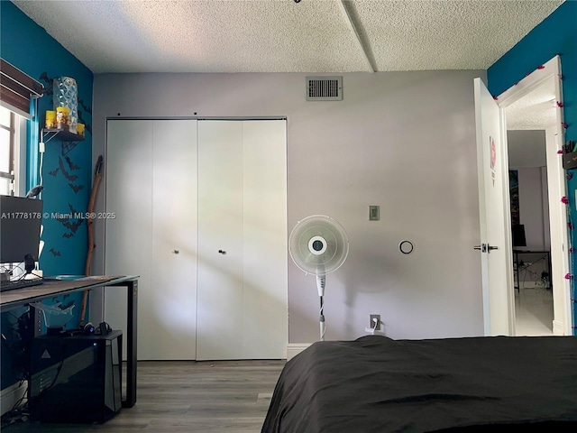 bedroom featuring visible vents, a closet, wood finished floors, and a textured ceiling