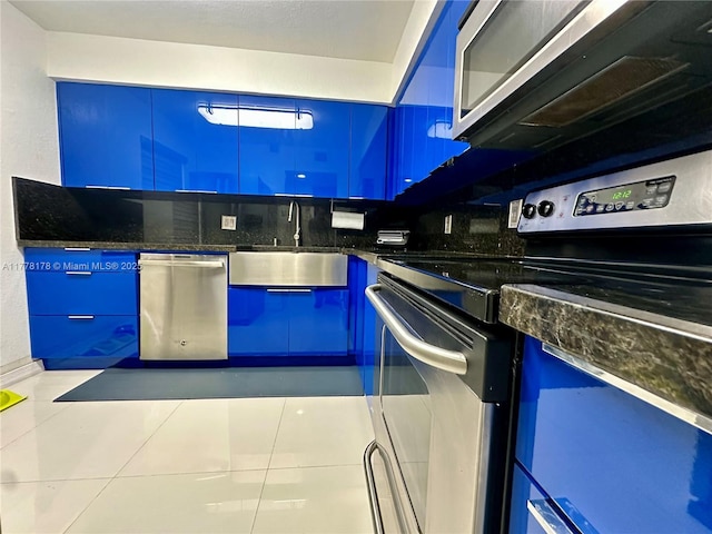 kitchen featuring dark stone countertops, appliances with stainless steel finishes, a sink, and blue cabinetry