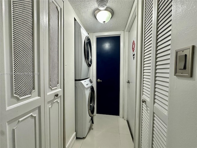 laundry area featuring light tile patterned floors, a textured ceiling, laundry area, and stacked washer and clothes dryer