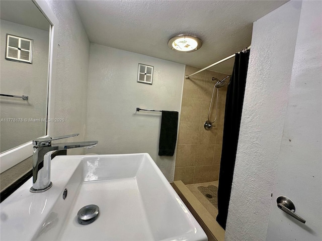 bathroom with a sink, a shower stall, a textured wall, and a textured ceiling