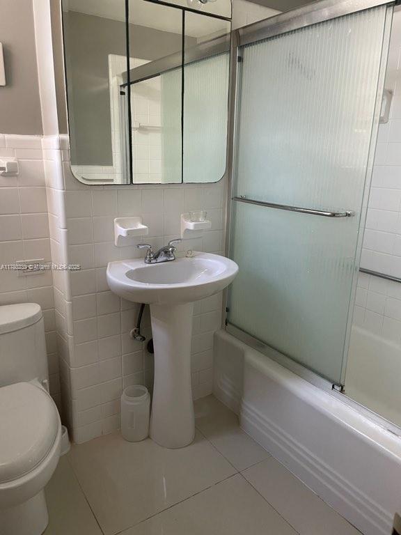 345 N Fort Lauderdale Beach Blvd Unit 202, Fort Lauderdale, FL 33304 - bathroom with tile patterned flooring, shower / bath combination with glass door, tile walls, and toilet