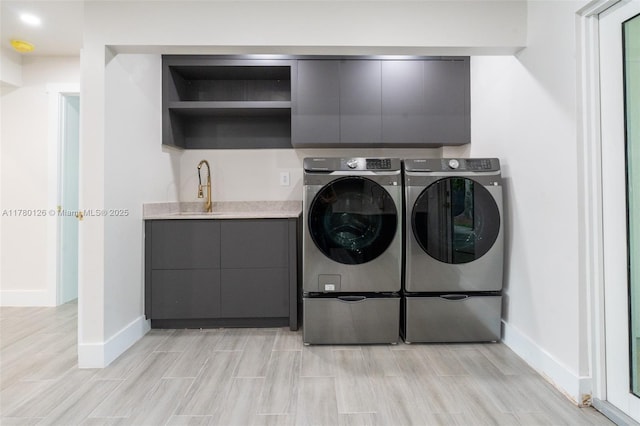 laundry room featuring a sink, wood tiled floor, baseboards, cabinet space, and washer and clothes dryer