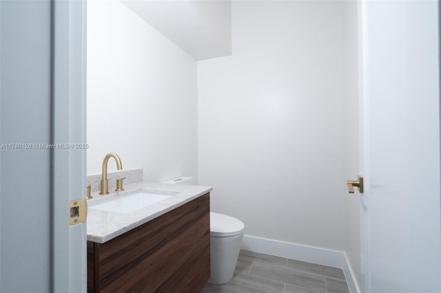half bath featuring toilet, baseboards, and vanity