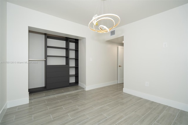 unfurnished room featuring a notable chandelier, baseboards, visible vents, and wood finish floors