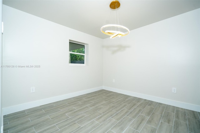 empty room with baseboards, wood finish floors, and a notable chandelier