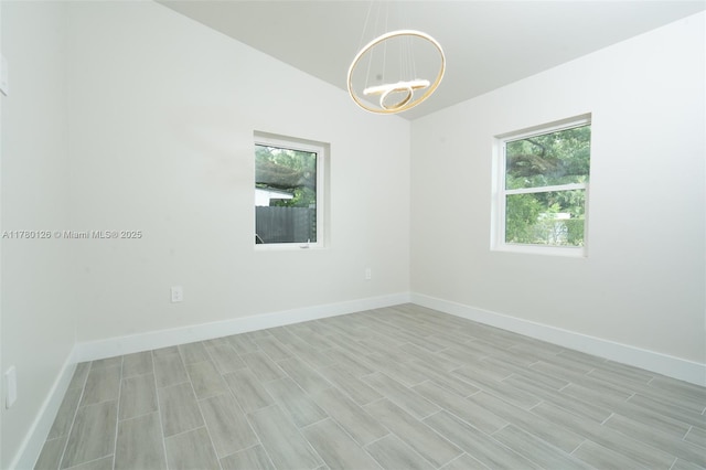 spare room featuring a healthy amount of sunlight, a notable chandelier, and baseboards