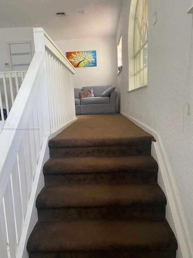 stairs with visible vents and a textured wall