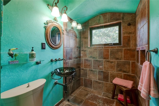 full bathroom with a tile shower, toilet, lofted ceiling, and a sink