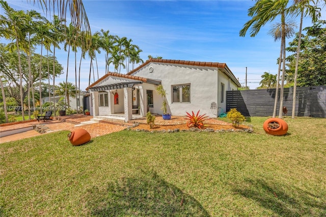 rear view of property featuring stucco siding, a tiled roof, fence, a pergola, and a lawn