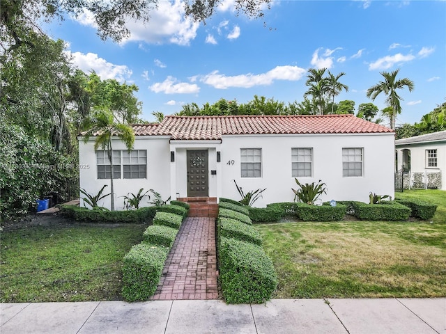 mediterranean / spanish house with a front yard, stucco siding, and a tile roof