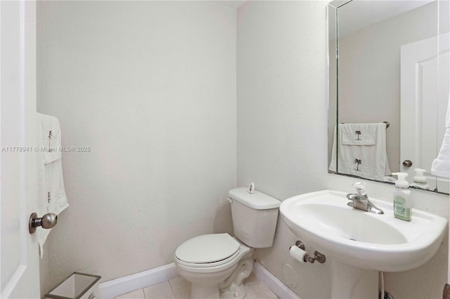 half bath with tile patterned floors, baseboards, a sink, and toilet
