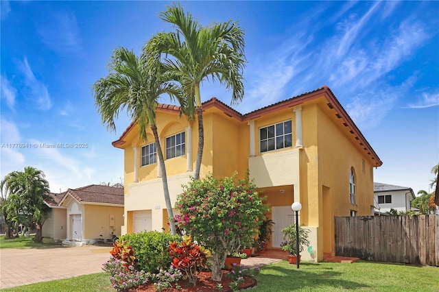 mediterranean / spanish-style house with a tiled roof, stucco siding, decorative driveway, fence, and a garage