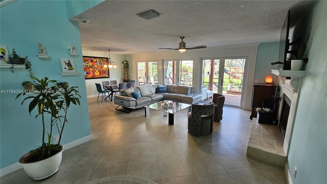 tiled living room with a textured ceiling, ceiling fan with notable chandelier, a fireplace, and baseboards