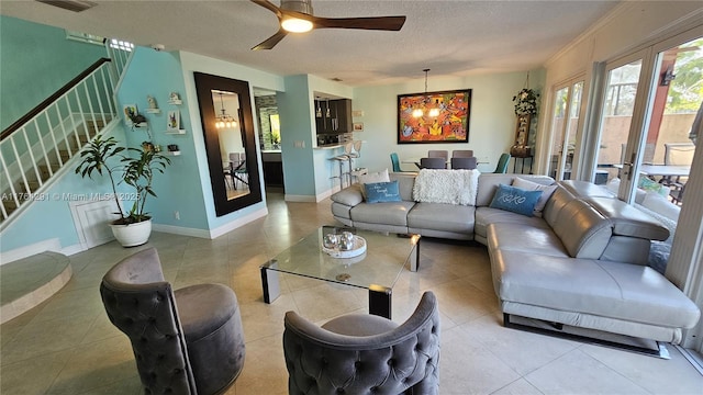 living area featuring ceiling fan with notable chandelier, a textured ceiling, stairway, tile patterned floors, and baseboards