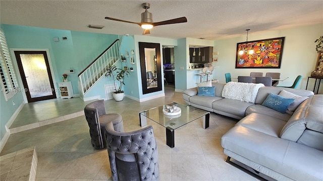 living area with visible vents, a ceiling fan, a textured ceiling, stairs, and tile patterned floors