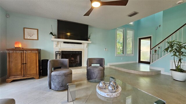 living area with ceiling fan, light tile patterned floors, visible vents, a tiled fireplace, and baseboards