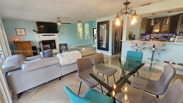 living room featuring stairway, light tile patterned flooring, a fireplace with raised hearth, visible vents, and ceiling fan