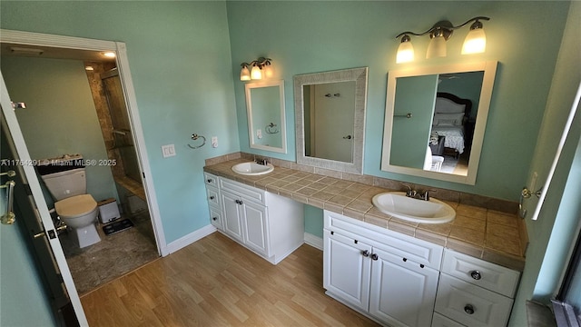 bathroom featuring toilet, wood finished floors, double vanity, and a sink