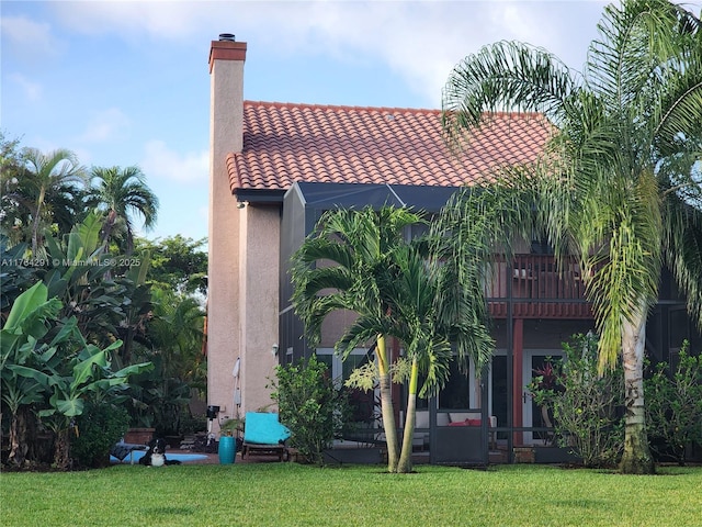 exterior space with a tiled roof, a yard, a chimney, a balcony, and stucco siding