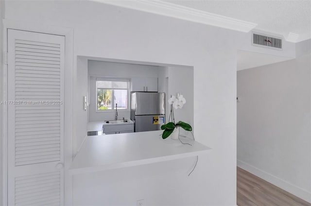 kitchen with wood finished floors, freestanding refrigerator, light countertops, a sink, and visible vents