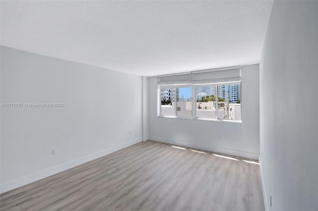 spare room featuring a textured ceiling, wood finished floors, and baseboards