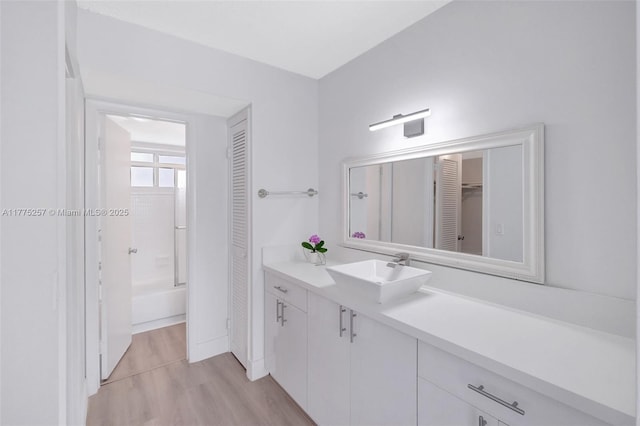 bathroom with a closet, a bathtub, wood finished floors, and vanity