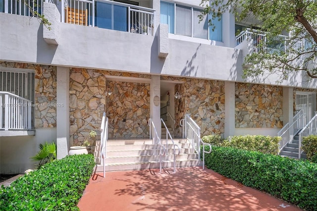 exterior space with stucco siding, a balcony, and stone siding