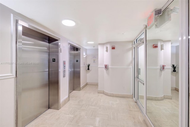 corridor with elevator, light floors, and baseboards