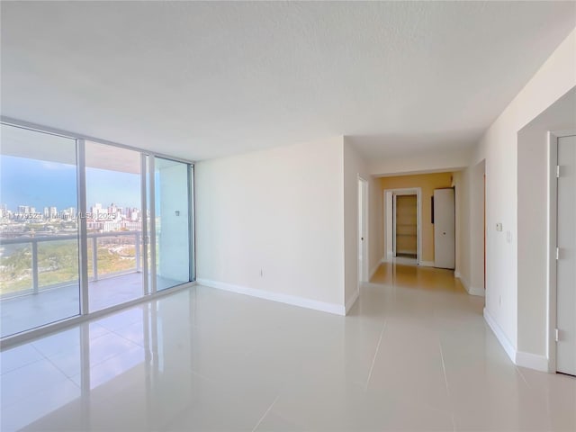 empty room with light tile patterned flooring, a view of city, baseboards, and a wall of windows