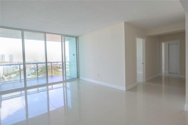 unfurnished room with a city view, light tile patterned floors, baseboards, and a wall of windows