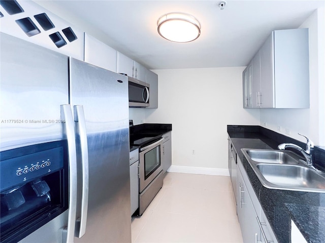 kitchen featuring appliances with stainless steel finishes, light tile patterned floors, a sink, and dark countertops