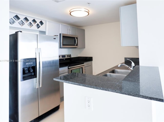 kitchen with a peninsula, gray cabinets, dark countertops, a sink, and stainless steel appliances