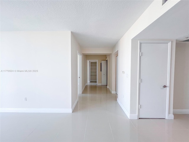 hall featuring a textured ceiling, light tile patterned floors, baseboards, and visible vents