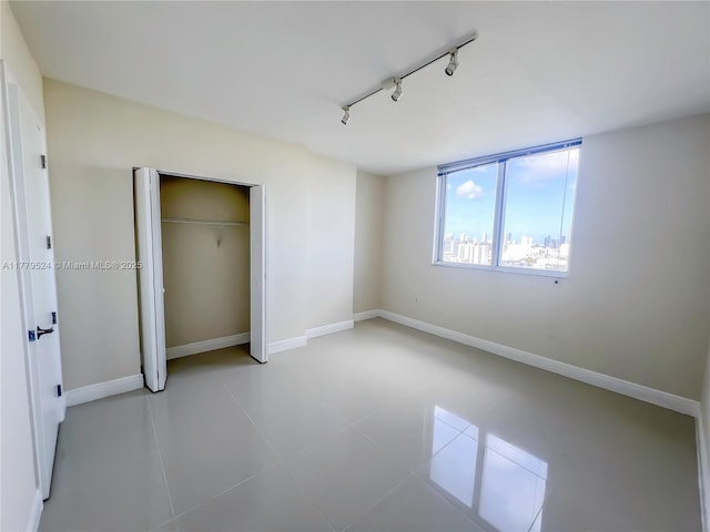unfurnished bedroom featuring a closet, baseboards, tile patterned flooring, and track lighting