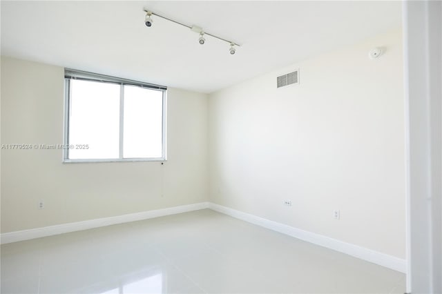 spare room featuring rail lighting, visible vents, and baseboards