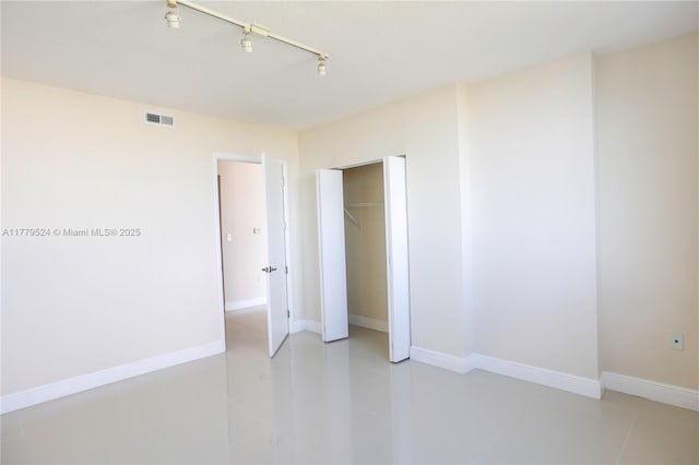 unfurnished bedroom featuring a closet, baseboards, track lighting, light tile patterned floors, and visible vents