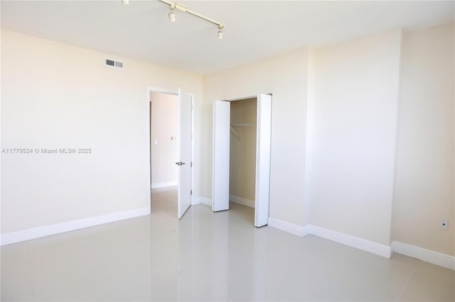 unfurnished bedroom with light tile patterned floors, rail lighting, a closet, visible vents, and baseboards
