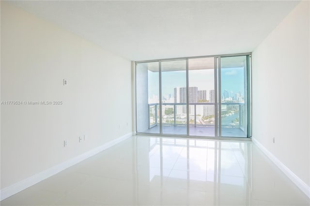 unfurnished room with a city view, tile patterned floors, baseboards, and floor to ceiling windows