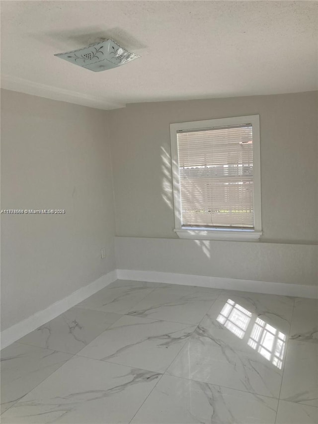 unfurnished room featuring baseboards, marble finish floor, and a textured ceiling