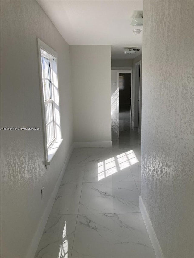 empty room with marble finish floor, a textured wall, and baseboards